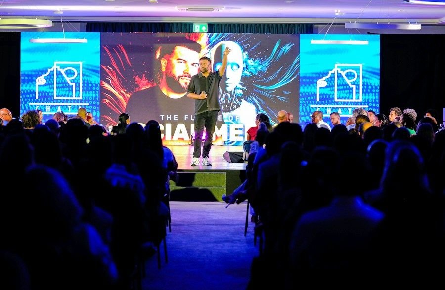 Işıklı sahnede konuşmacı ve kalabalık izleyiciler